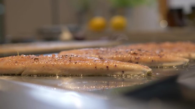 Extreme close-up handheld shot of Saibling Char fish fillets sizzling on a griddle covered in seasoning