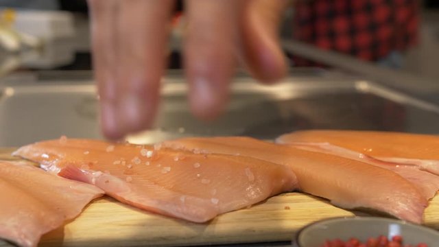 Handheld push-in shot of a chef seasoning slices of fillet Saibling Char fish with a sea salt rub on a kitchen counter