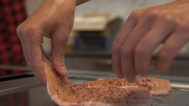 Handheld close-up shot of hands laying down slices of Saibling char fish fillets on a griddle
