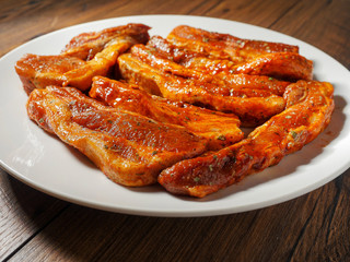 Pork belly slices in barbecue marinate on a white plate.