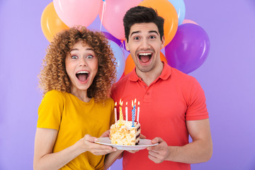 Image of excited couple man and woman celebrating birthday with multicolored air balloons and piece...