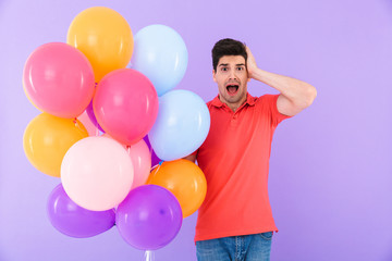 Fototapeta na wymiar Image of stressed caucasian man expressing panic while standing with multicolored air balloons