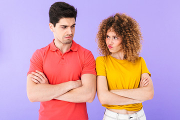 Fototapeta premium Portrait of angry young couple man and woman in basic t-shirts standing with arms folded in quarrel