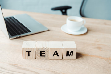 selective focus of team lettering on wooden cubes near laptop and cup with coffee