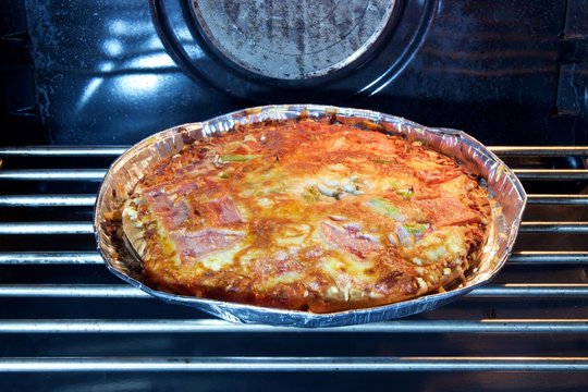 Close Up hot freshly baked homemade pizza in the oven in an aluminum plate. Yummy with melted cheese tomato sauce ham and pepper ready to eat at the house party