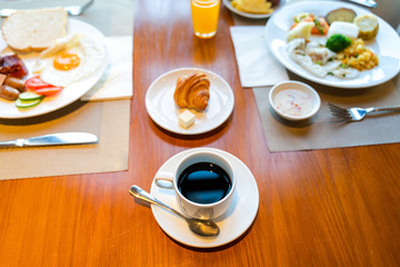 Fresh breakfast table next to window with bread, pastry, egg, fruit, juice, coffee cup
