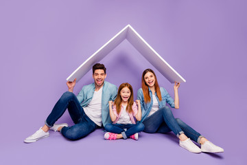 Portrait of three family members sitting floor under new roof wear casual clothes isolated purple...