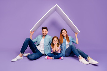 Family portrait of three members sitting floor under new roof wear casual clothes isolated purple...