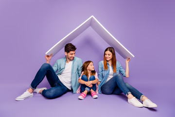 Family portrait of three members sitting floor under new roof wear casual clothes isolated purple background