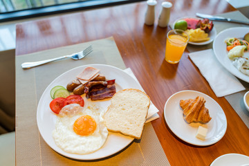 Fresh breakfast table next to window with bread, pastry, egg, fruit, juice, coffee cup