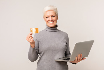 Smiling senior woman holding credit card and laptop