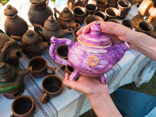 Close up of woman hands with purple ceramic kettle at art souvenir market. Handmade, art and handicraft concept