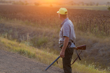  Hunting period, autumn season open. A hunter with a gun in his hands in hunting clothes in the autumn forest in search of a trophy. A man stands with weapons and hunting dogs tracking down the game.