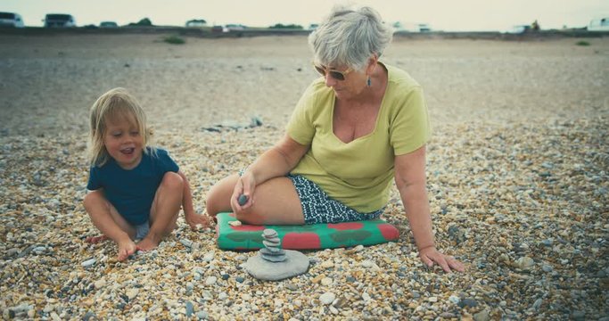 Little toddler playing with grandmother on beach