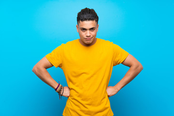 Young man with yellow shirt over isolated blue background angry