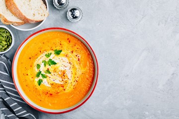 Carrot and pumpkin cream soup with parsley on gray stone background.