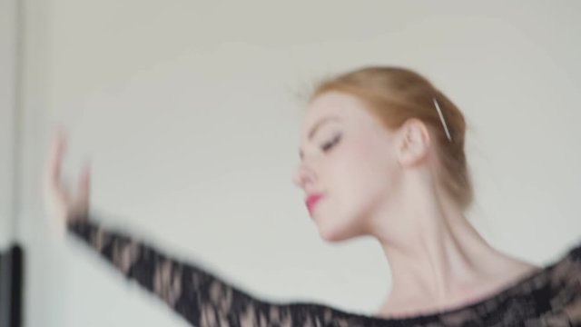 Zoom in of graceful redhead ballerina in black lace leotard rehearsing dance in ballet studio, closeup head and shoulders shot