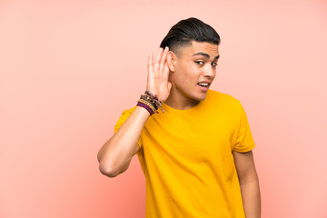 Young man with yellow shirt over isolated pink wall listening something