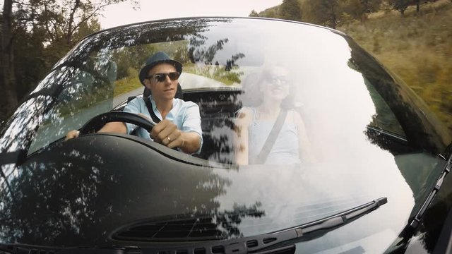 4K smiling couple riding in RHD convertible with man at wheel and woman pointing at something