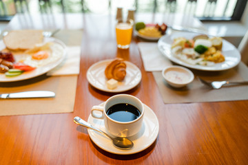 Fresh breakfast table next to window with bread, pastry, egg, fruit, juice, coffee cup