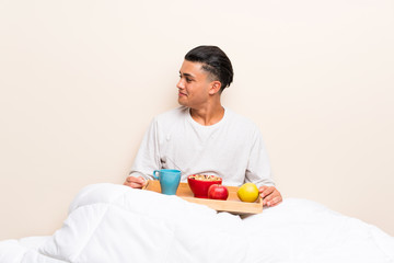 Young man having breakfast in bed looking to the side