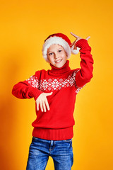 Boy in Santa hat and red sweater having fun on Christmas day against yellow background