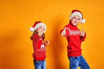 Happy children in red sweaters with deer having fun and showing thumbs up on Christmas day against yellow background