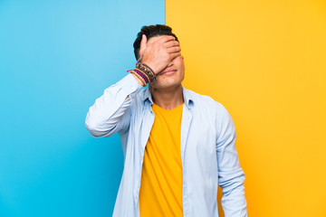 Young man over isolated colorful background covering eyes by hands