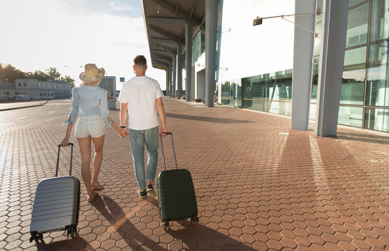 Couple walking near airport building with luggage