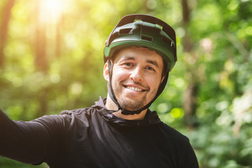 Happy smiling cyclist man taking selfie in green forest
