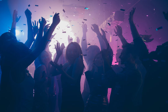 Close up photo of many party people dancing purple lights confetti flying everywhere nightclub event hands raised up wear shiny clothes