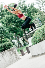 Full-length portrait of young woman trail runner jumping while having workout in city park. Vertical shot. Dutch angle