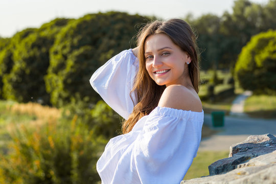 Young beautiful woman with bare shoulders in white clothes in the park