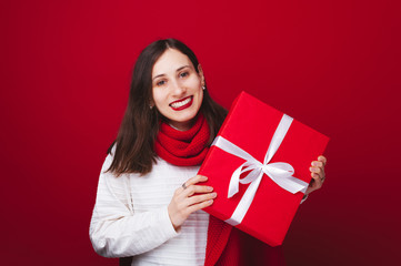 Fototapeta premium Beautiful young woman holding big red gift over red background