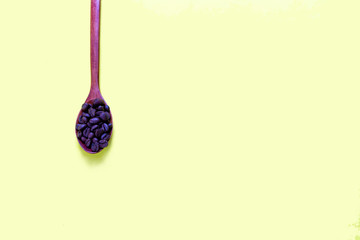 Coffee beans in a wooden spoon on a yellow background