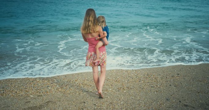Young mother carrying toddler walking to the water on beach