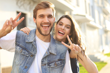 Image of a happy smiling cheerful young couple outdoors take a selfie by camera showing peace.