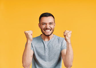 Happy man celebrating his success with winner gesture on yellow background