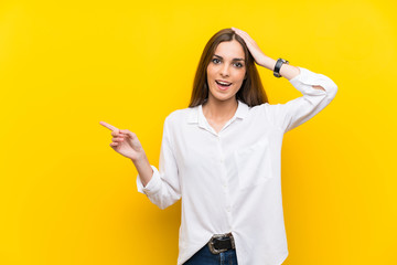 Young woman over isolated yellow background surprised and pointing finger to the side