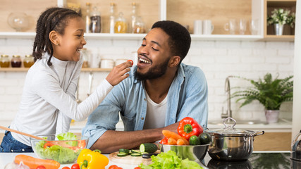 Naklejka premium Lovely afro girl giving her dad tomato to taste