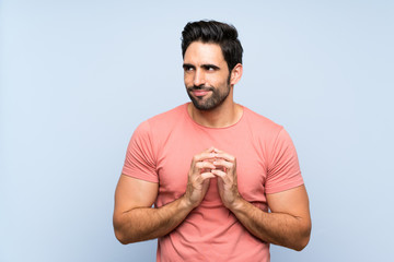 Handsome young man in pink shirt over isolated blue background scheming something