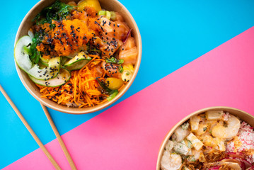 Flat lay composition with prawn poke and salmon poke on a blue and pink background with chopsticks