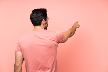 Handsome young man over isolated pink background pointing back with the index finger