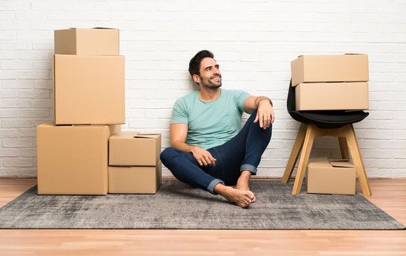 Handsome young man moving in new home among boxes laughing and looking up