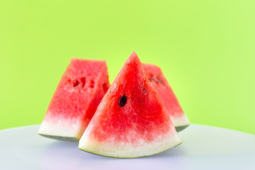 Close up slices of fresh red watermelon on white plate with green background.
