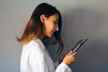 Fototapeta premium Medicine Concept: Young female doctor on a gray background using a digital tablet.