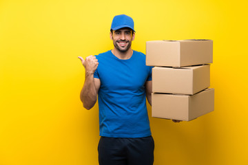 Fototapeta na wymiar Young delivery man over isolated yellow wall pointing to the side to present a product