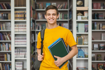 Handsome young guy standing in library, bookshelves background