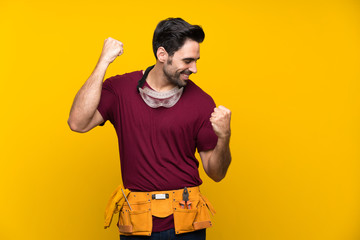 Handsome young craftsman over isolated yellow background celebrating a victory