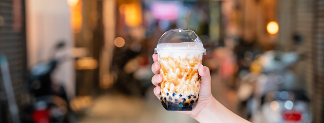 Young girl is holding and showing a cup of brown sugar flavored tapioca pearl bubble milk tea in...